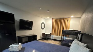 A hotel room with a large bed, a desk with a chair, a television, and a window with curtains.
