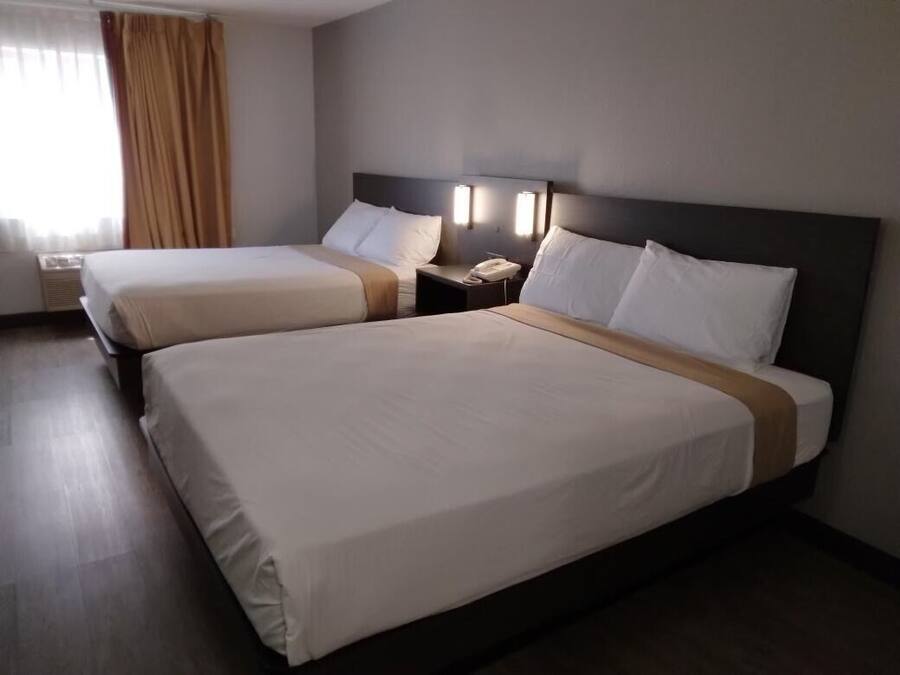 Ein Hotelzimmer mit zwei Betten, einem Nachttisch mit Telefon und einem Fenster mit Vorhängen.
