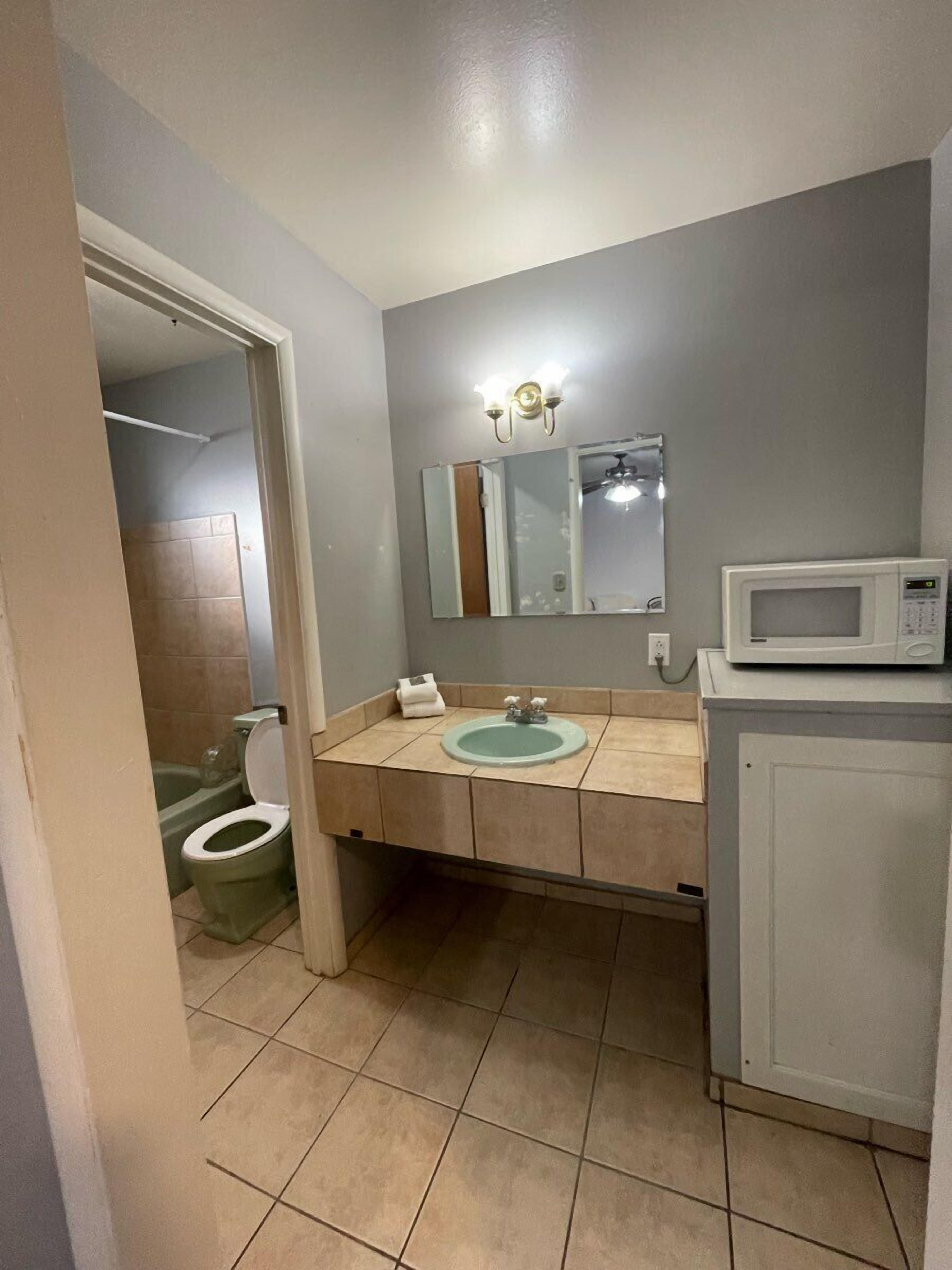 Un baño con inodoro, lavabo, espejo y un microondas sobre un mueble.