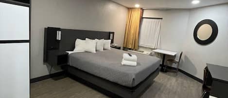 Una habitación de hotel moderna con cama, mesita de noche, escritorio y armario.