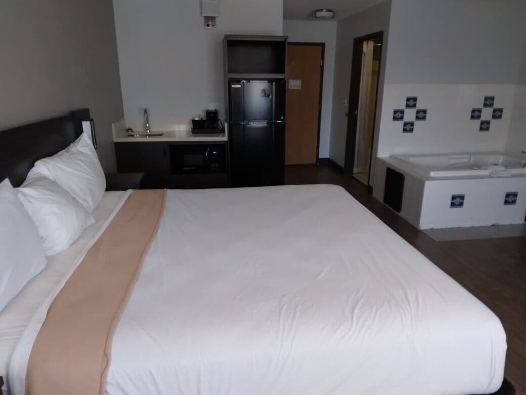 A hotel room with a large bed, a desk with a refrigerator, a sink, and a small bathroom area.