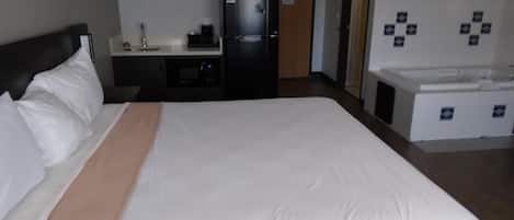 A hotel room with a large bed, a desk with a refrigerator, a sink, and a small bathroom area.