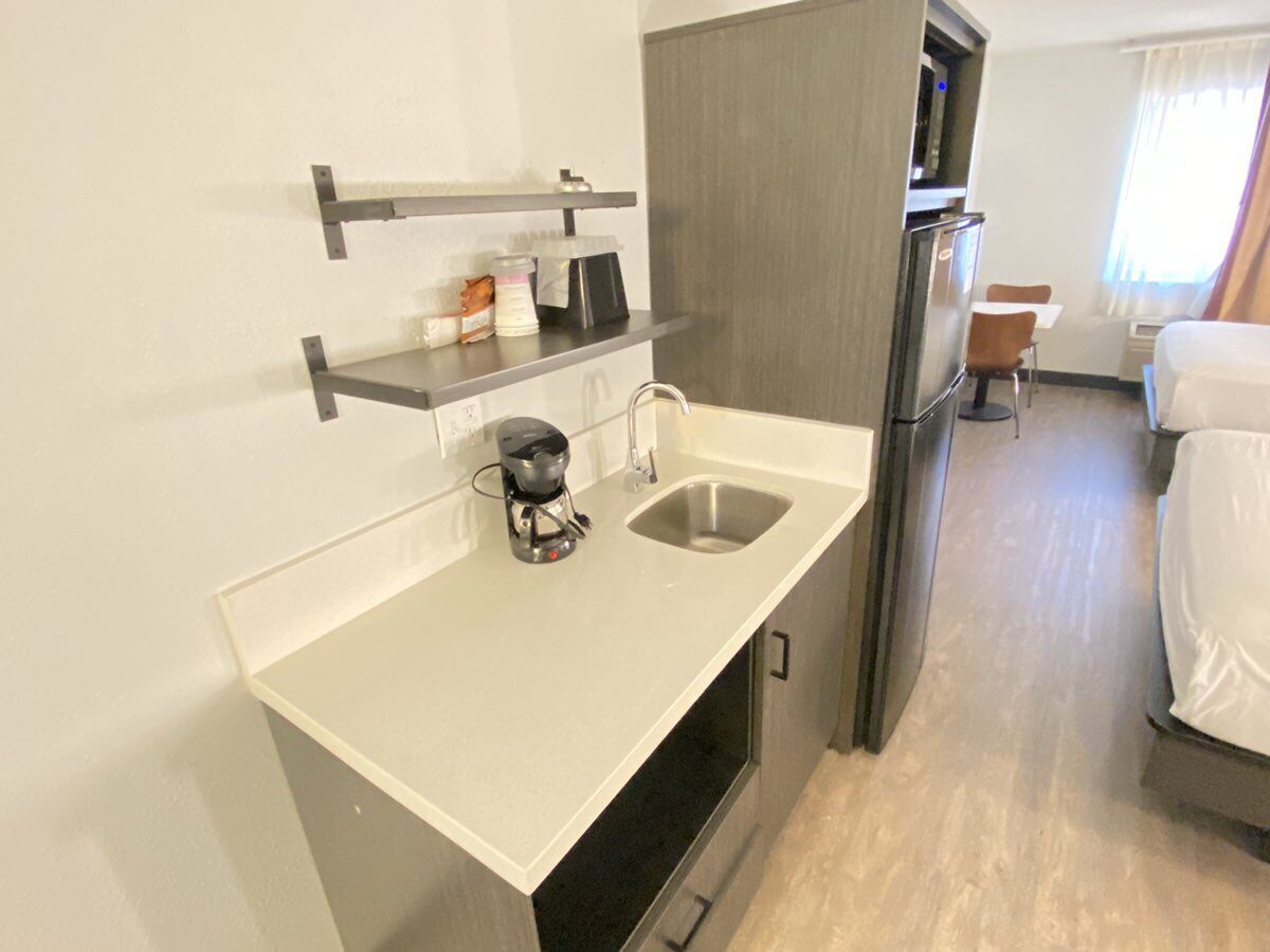 A compact hotel room with a kitchenette, a single bed, and a small seating area.