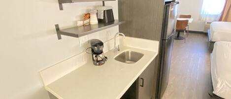 A compact hotel room with a kitchenette, a single bed, and a small seating area.