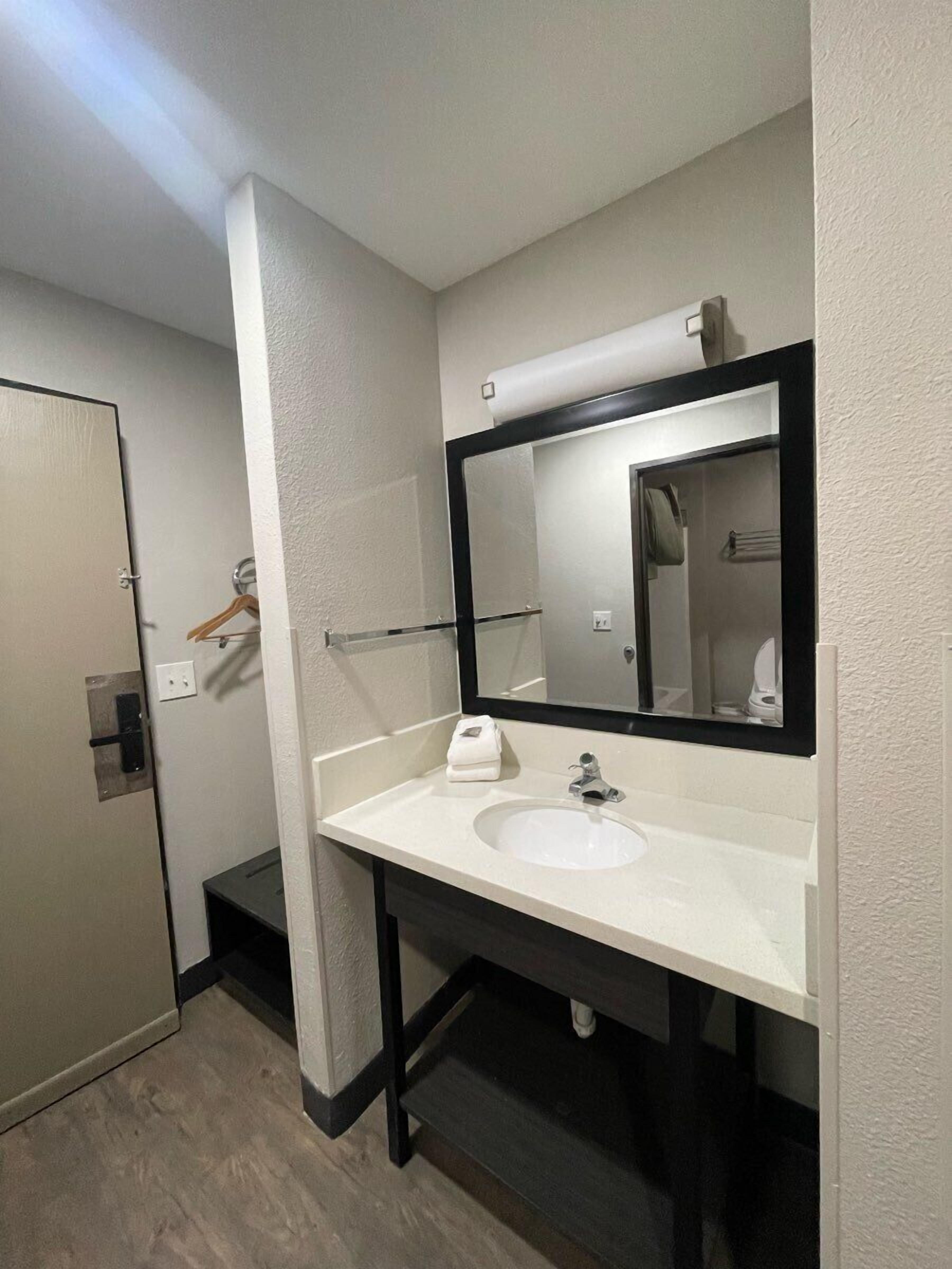Un baño con un lavamanos blanco, un espejo con marco negro y un perchero para toallas.
