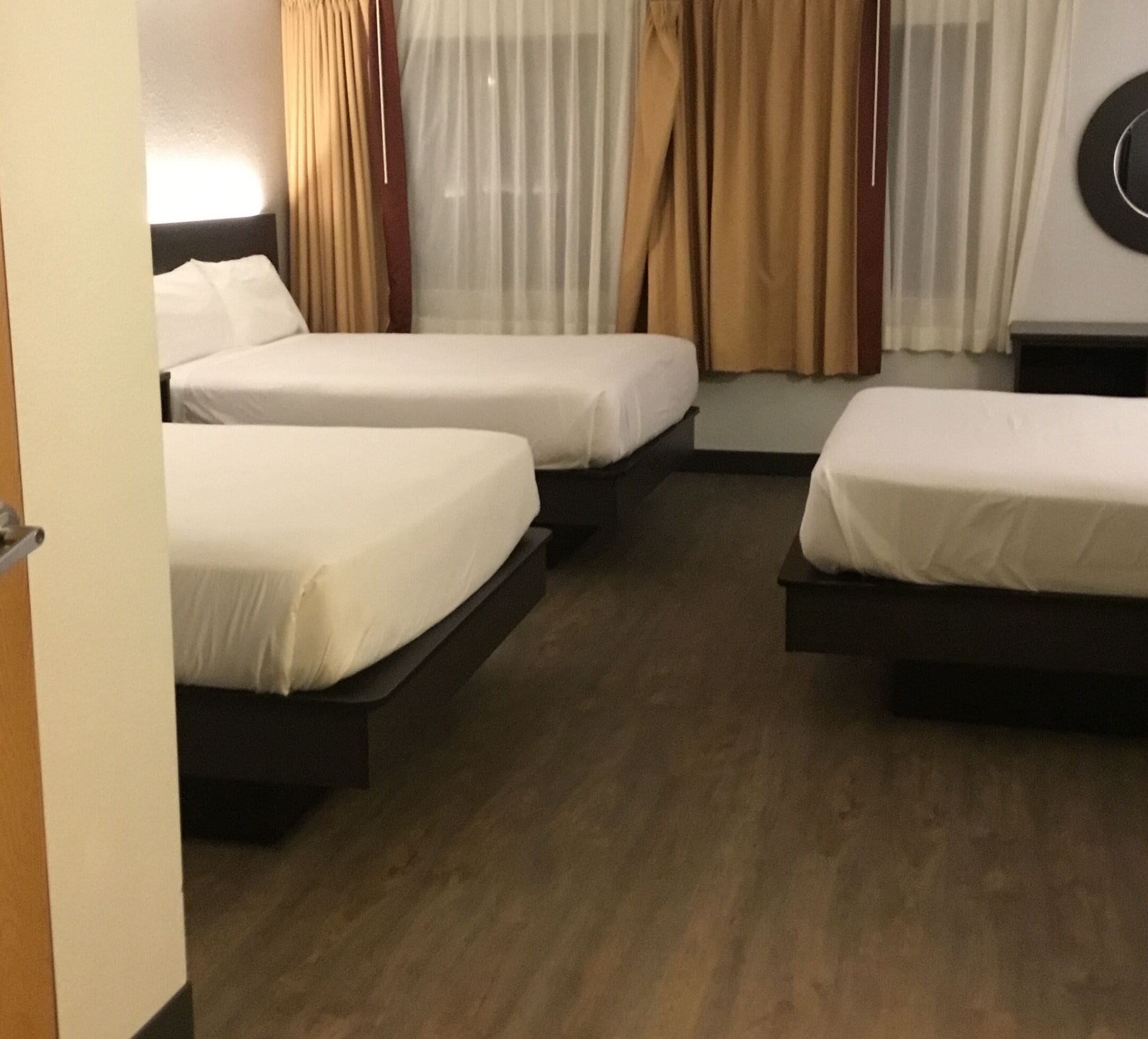 Una habitación de hotel con dos camas individuales, un ventanal con cortinas de encaje y piso de madera.