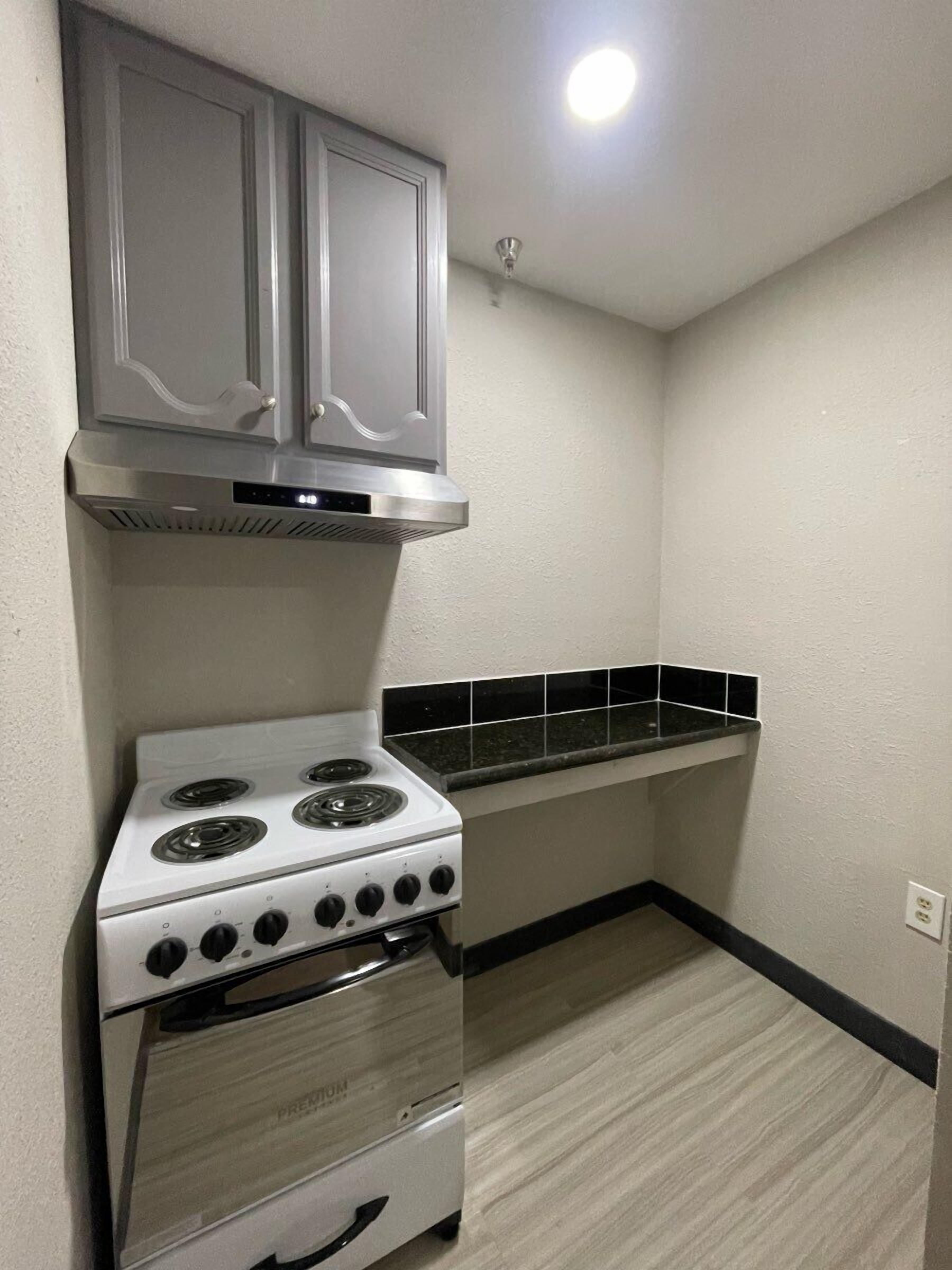 Uma cozinha compacta com fogão branco, painel atrás do fogão em azulejos pretos e coifa de aço inoxidável.