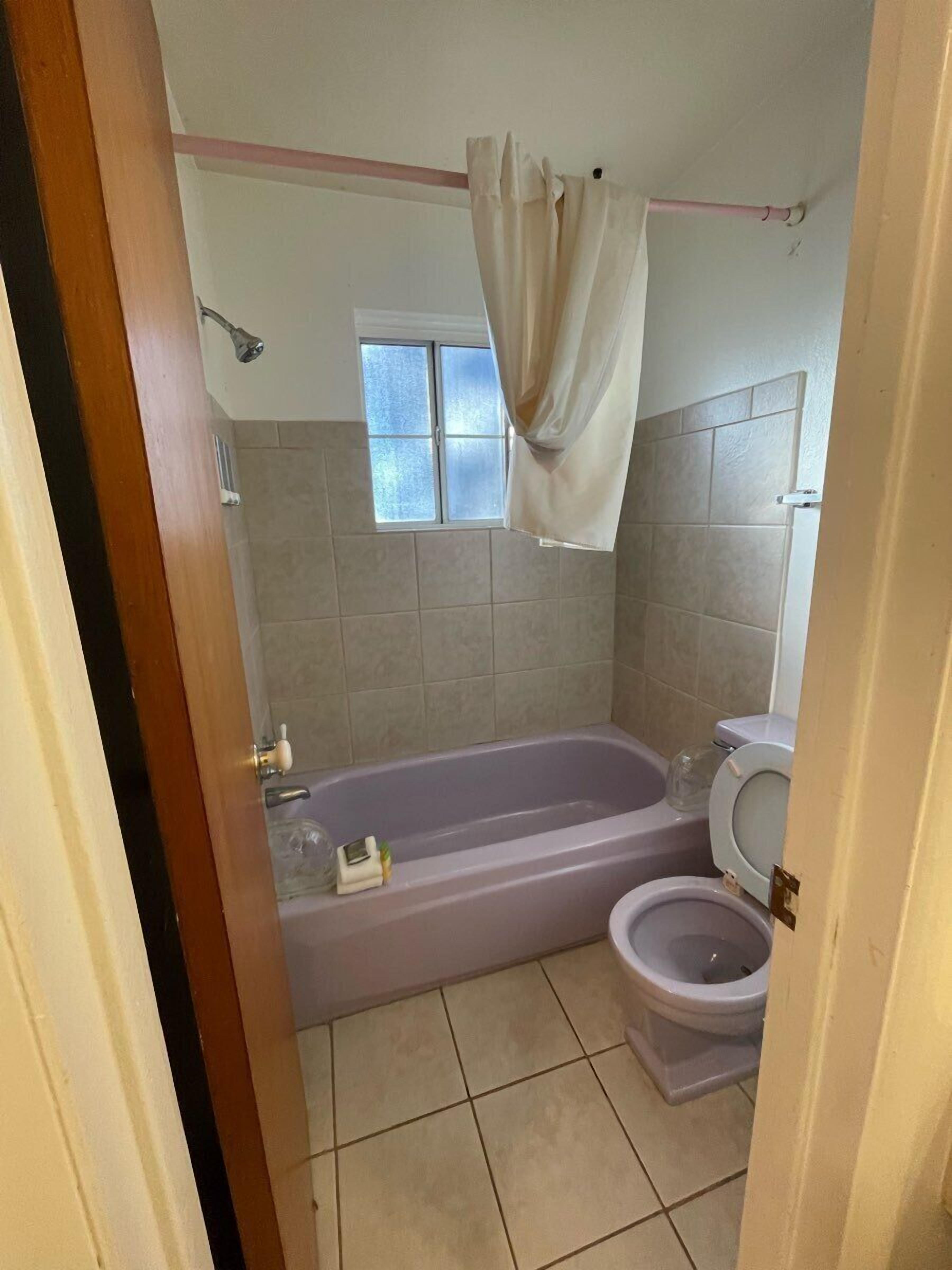 A bathroom with a bathtub, toilet, and a window.