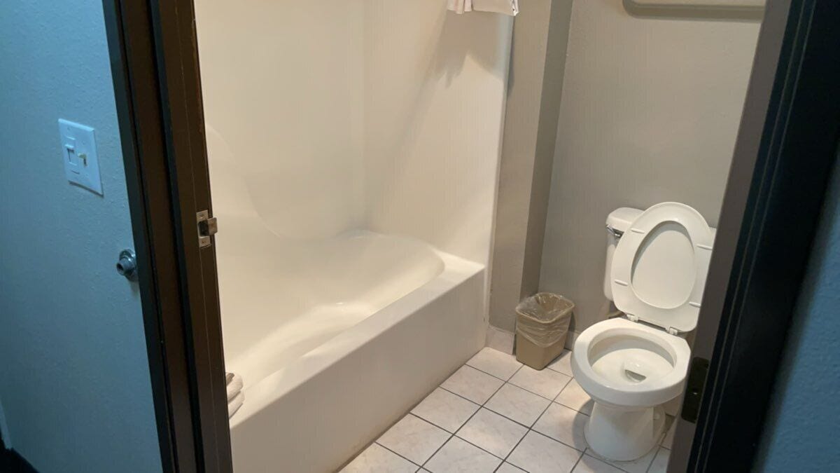 A bathroom with a bathtub, toilet, and a trash bin.