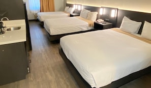Habitación de hotel con tres camas, un escritorio pequeño y un lavamanos.
