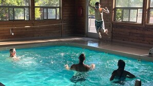 A swimming pool with wooden walls and large windows, surrounded by people swimming.