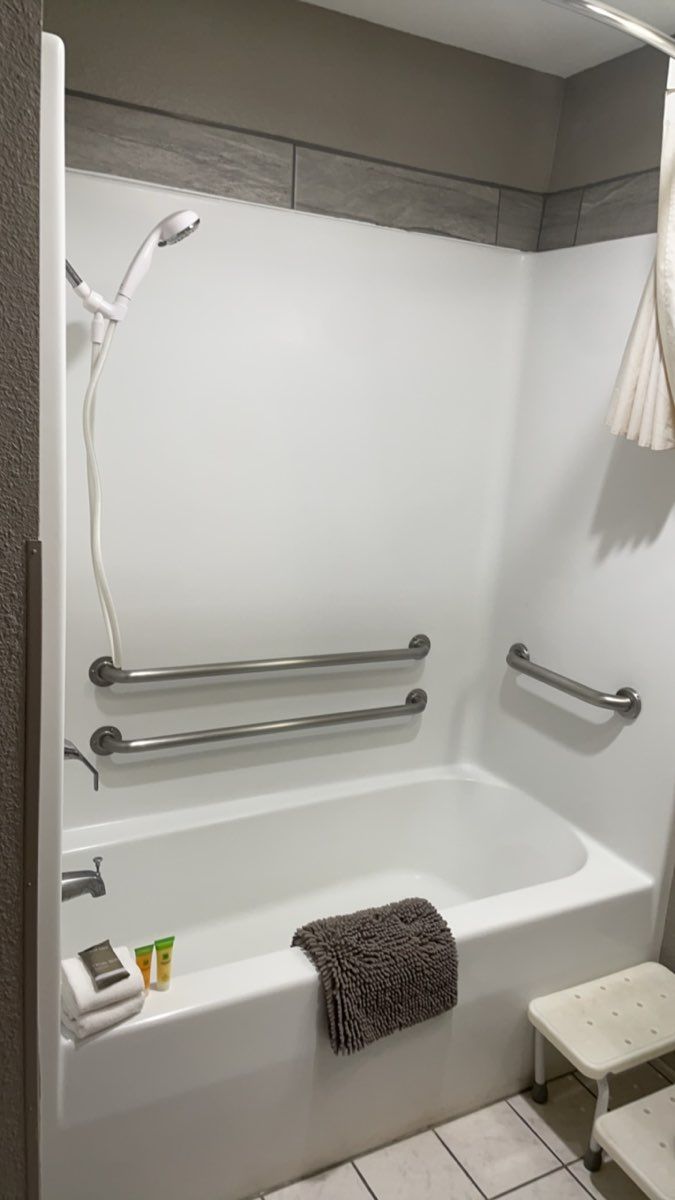 A bathroom with a white bathtub, grab bars, a towel rack, and a small stool.