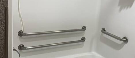 A bathroom with a white bathtub, grab bars, a towel rack, and a small stool.