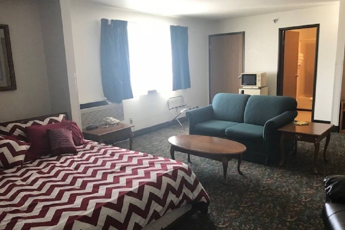 Et hotelværelse med seng, sofa, lille bord, fjernsyn og dør til badeværelse.