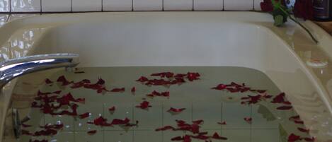 Une baignoire remplie d’eau dans laquelle flottent des pétales de rose, une bouteille de champagne et une bouteille de vin posées sur le bord.