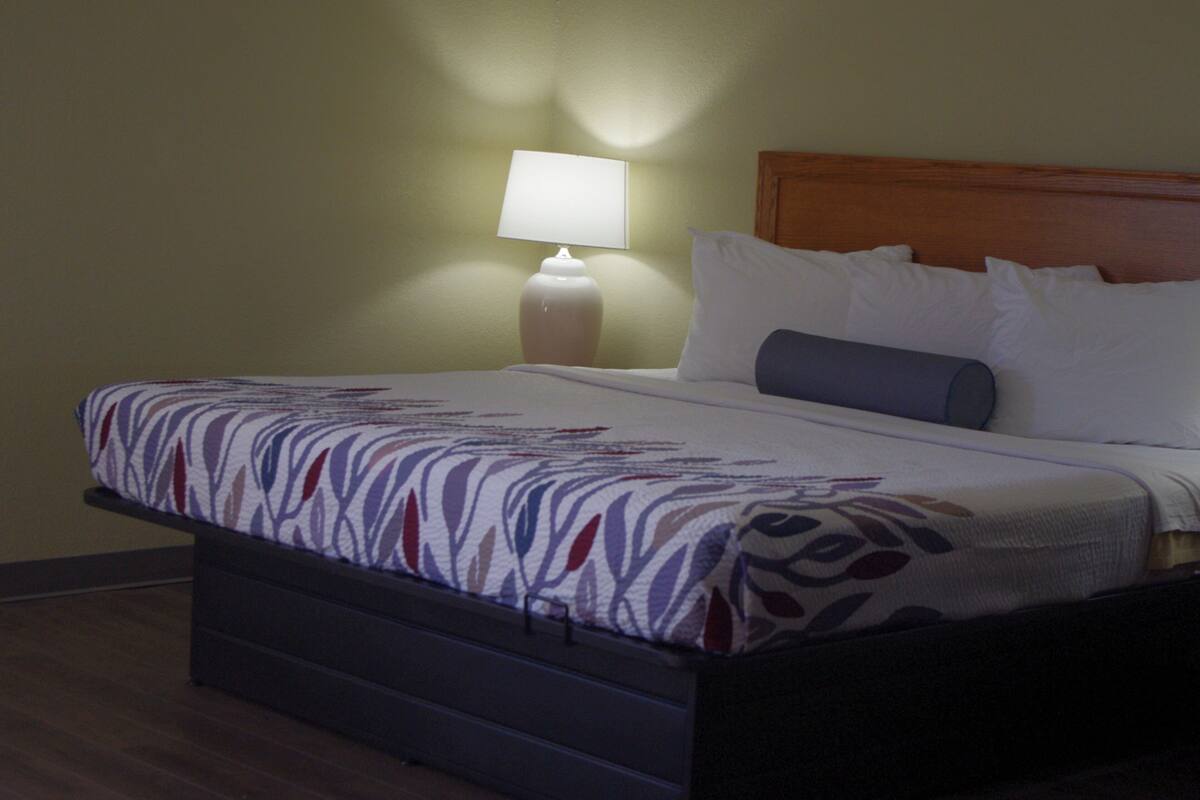 Et hotelværelse med seng, natbord med lampe og trægavl.