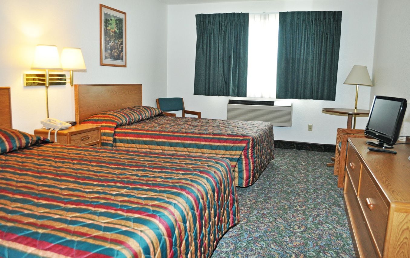 Habitación de hotel con dos camas, un escritorio, una silla, un televisor y una ventana con cortinas.