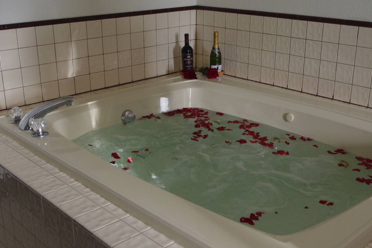 Et badekar fyldt med vand og rosenblade, med to flasker vin på kanten.