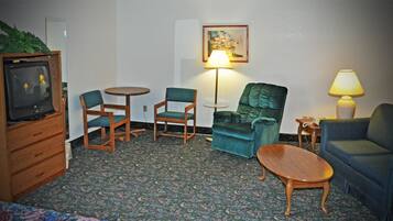 A hotel room with a television, two chairs, a sofa, a small table, a lamp, and a painting on the wall.