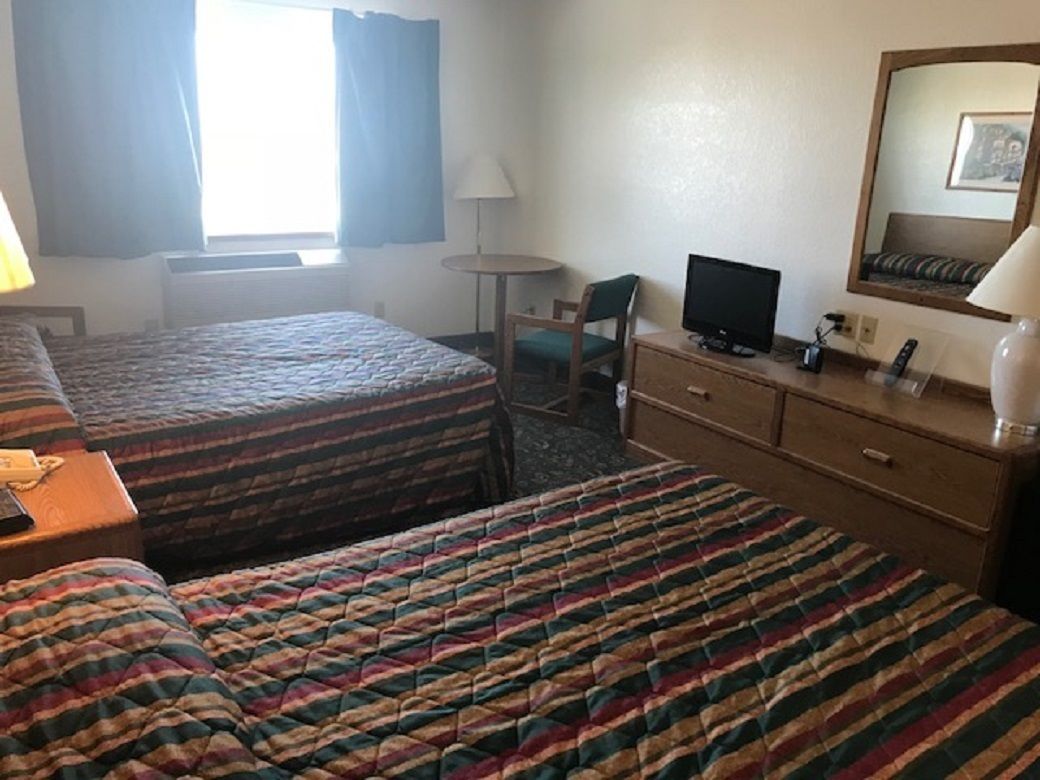 A hotel room with two beds, a desk with a computer, a chair, a lamp, and a mirror.