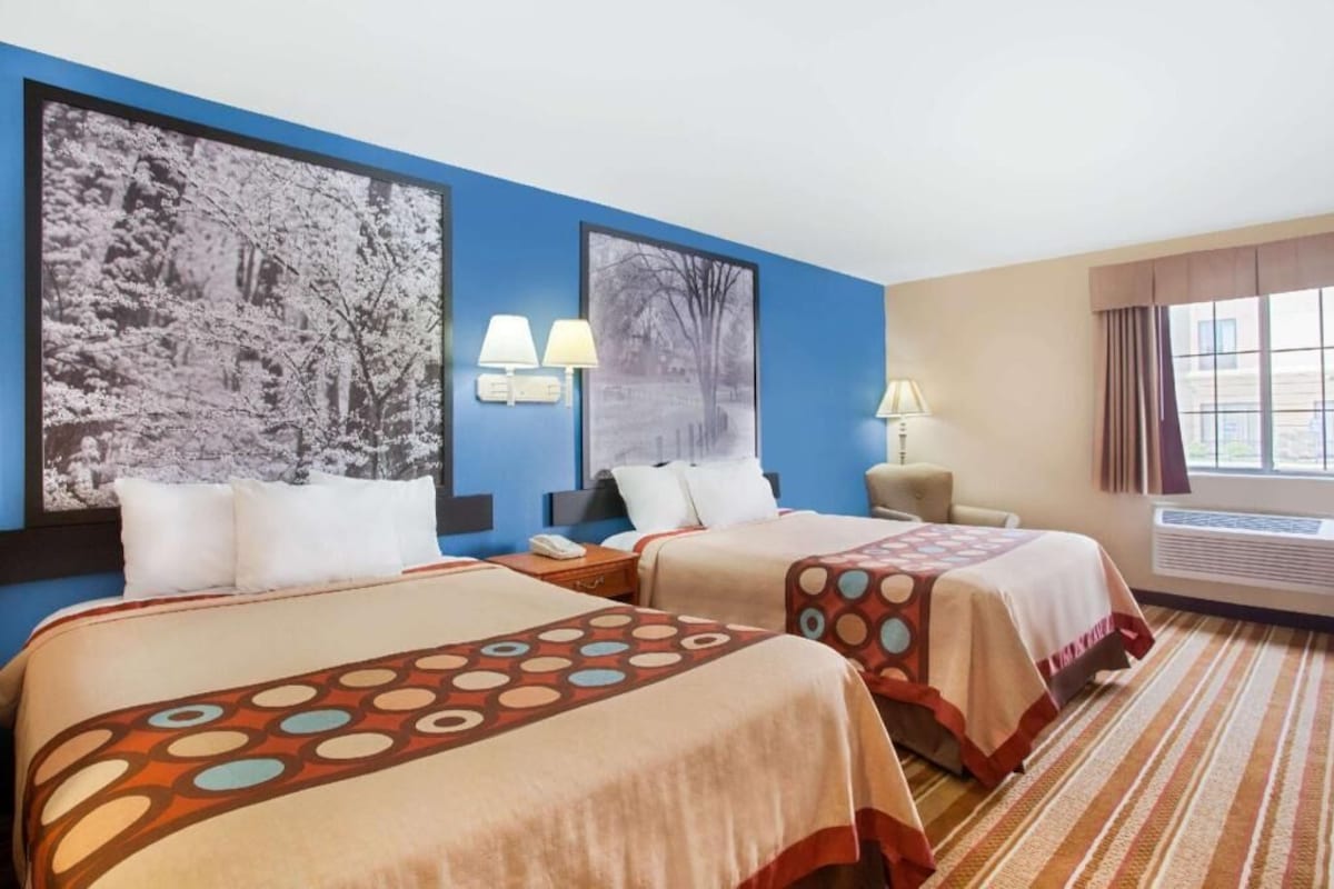 Habitación de hotel con dos camas, una mesita de noche, una lámpara y una ventana con cortinas.