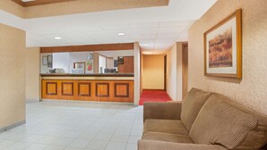 Un hall d’hôtel avec un comptoir d’accueil, un canapé marron et un tableau encadré au mur.