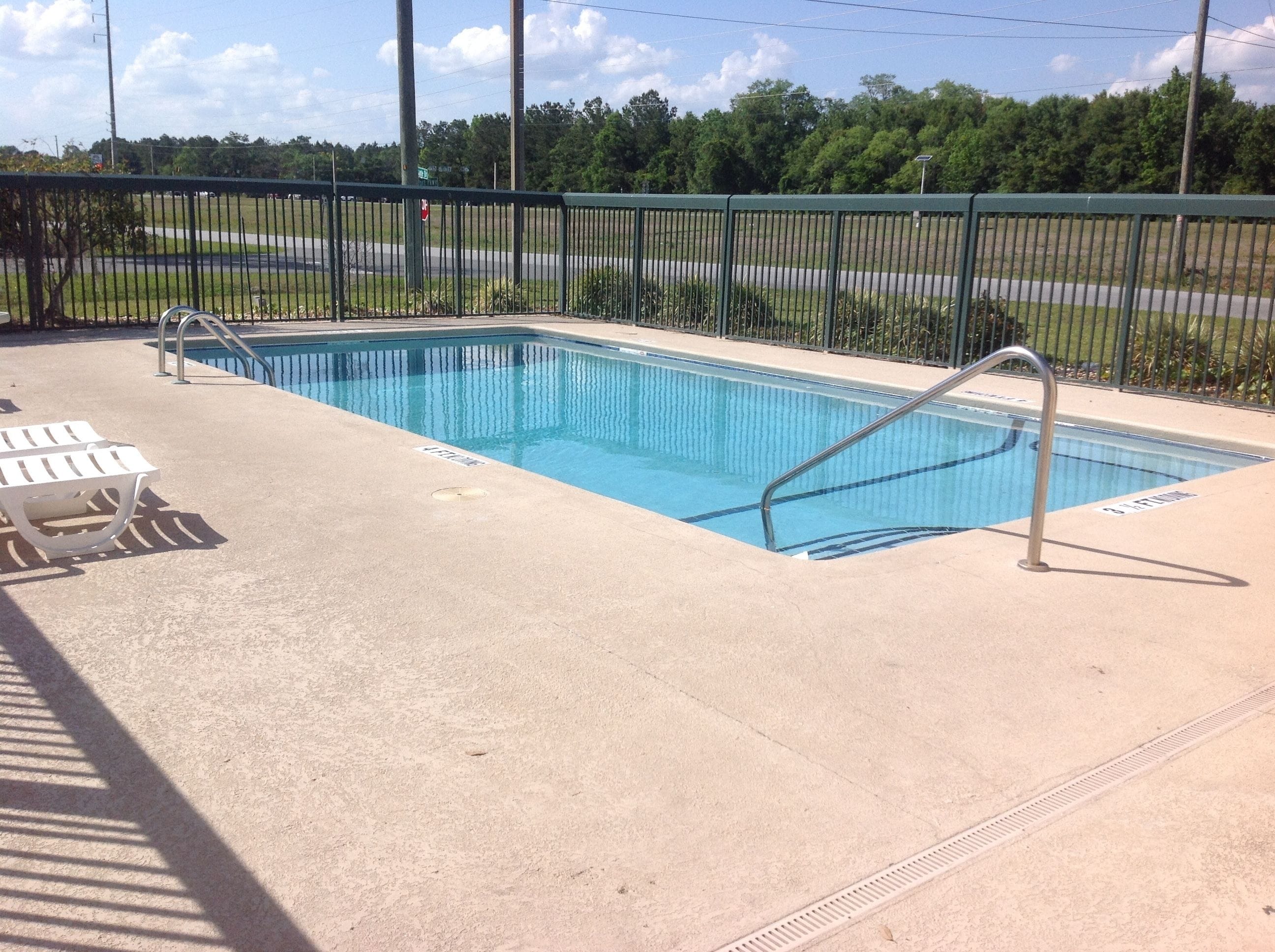 Una piscina rectangular con una escalera metálica y dos sillas reclinables blancas.