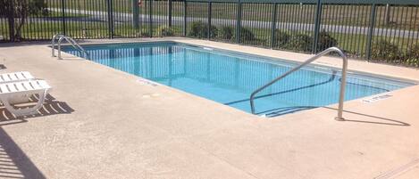 Una piscina rectangular con una escalera metálica y dos sillas reclinables blancas.