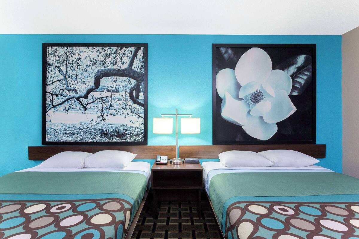 A hotel room with two beds, a nightstand, a lamp, and two framed pictures on the wall.