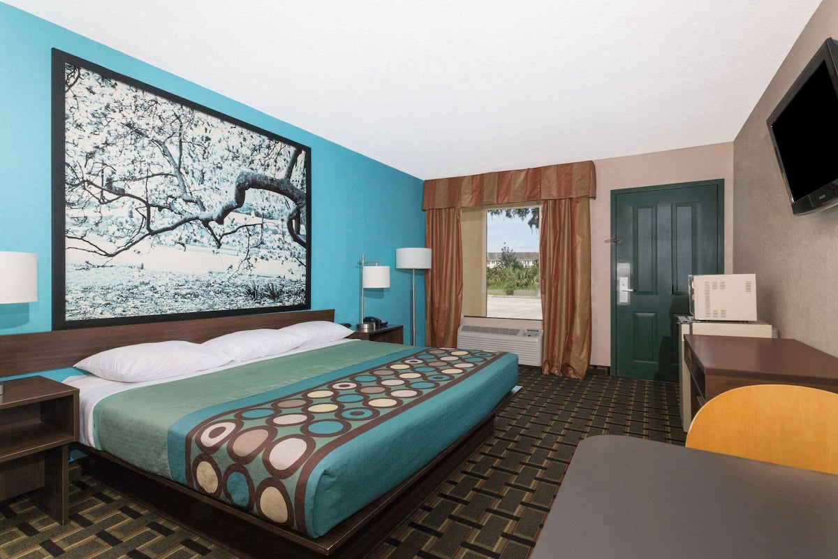 A hotel room with a large bed, a desk, a chair, a television, and a window with curtains.