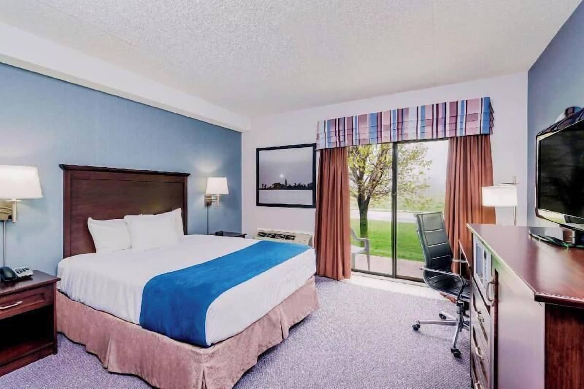 A hotel room with a bed, desk, chair, TV, and a view of the outdoors.