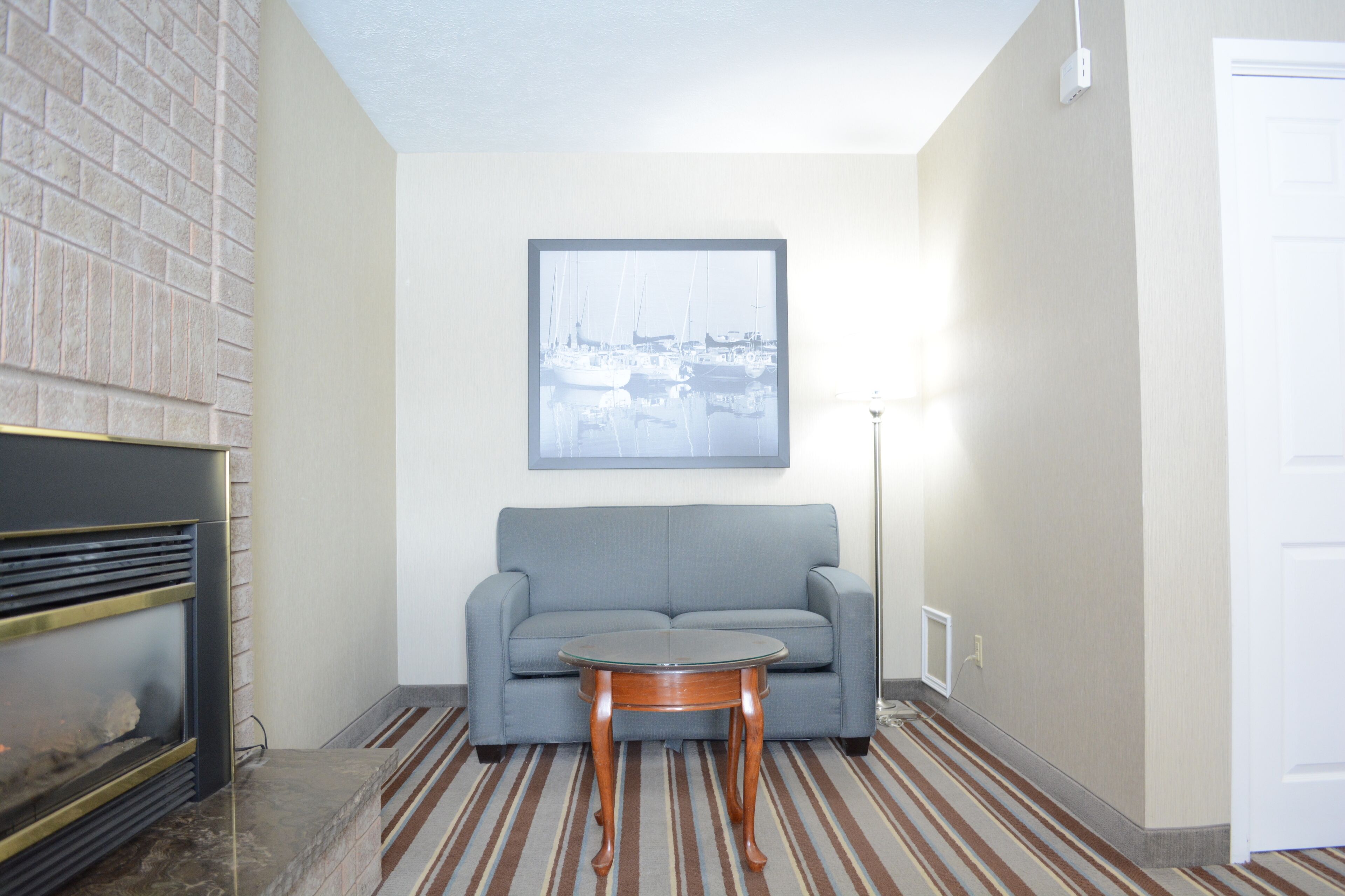 A modern living room with a gray sofa, a round wooden coffee table, and a framed cityscape picture on the wall.