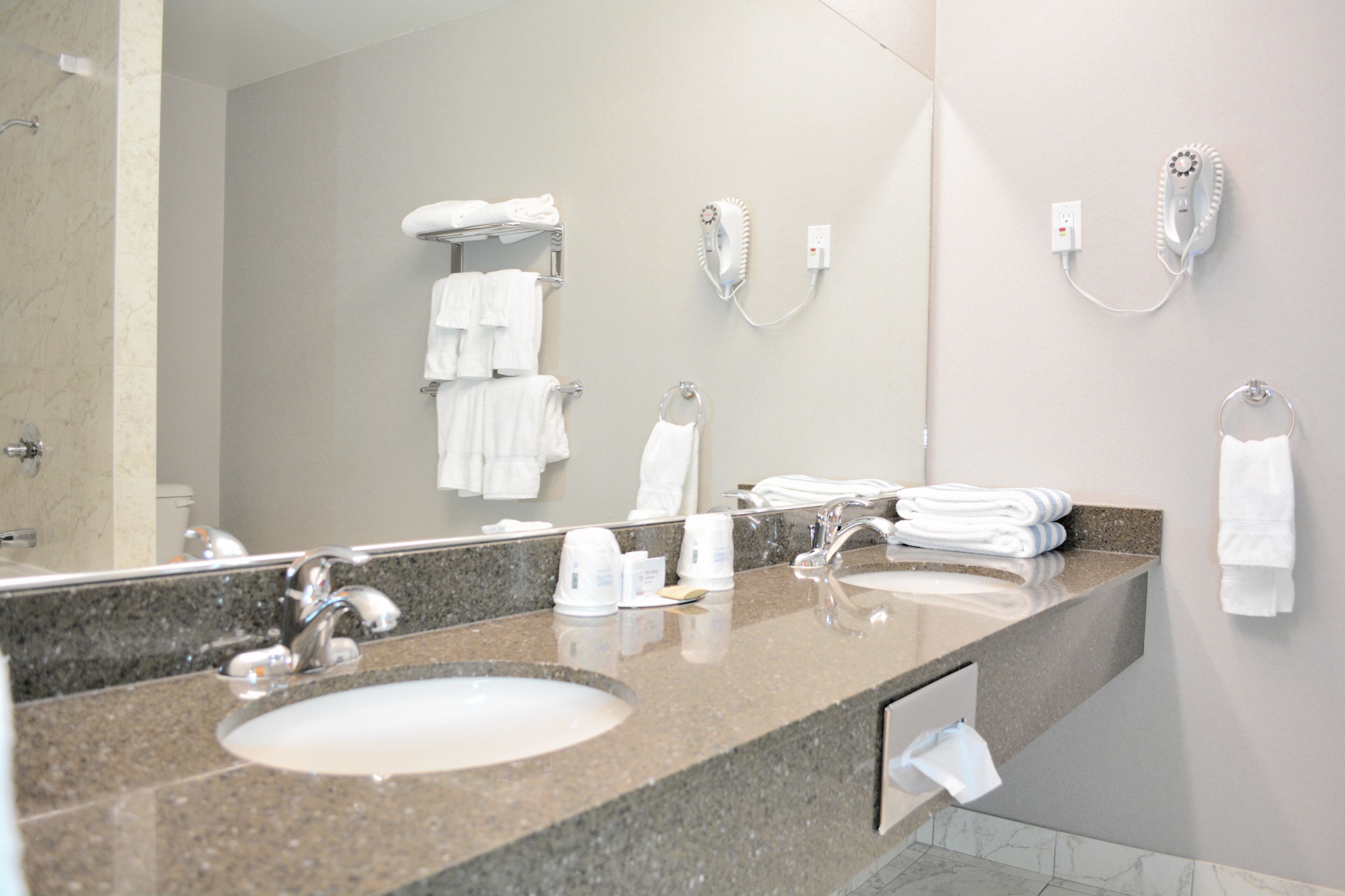A modern bathroom with dual sinks, a large mirror, and a towel rack with multiple towels.