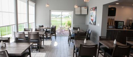 A spacious indoor dining area with multiple tables and chairs, large windows, and a view of the outdoors.