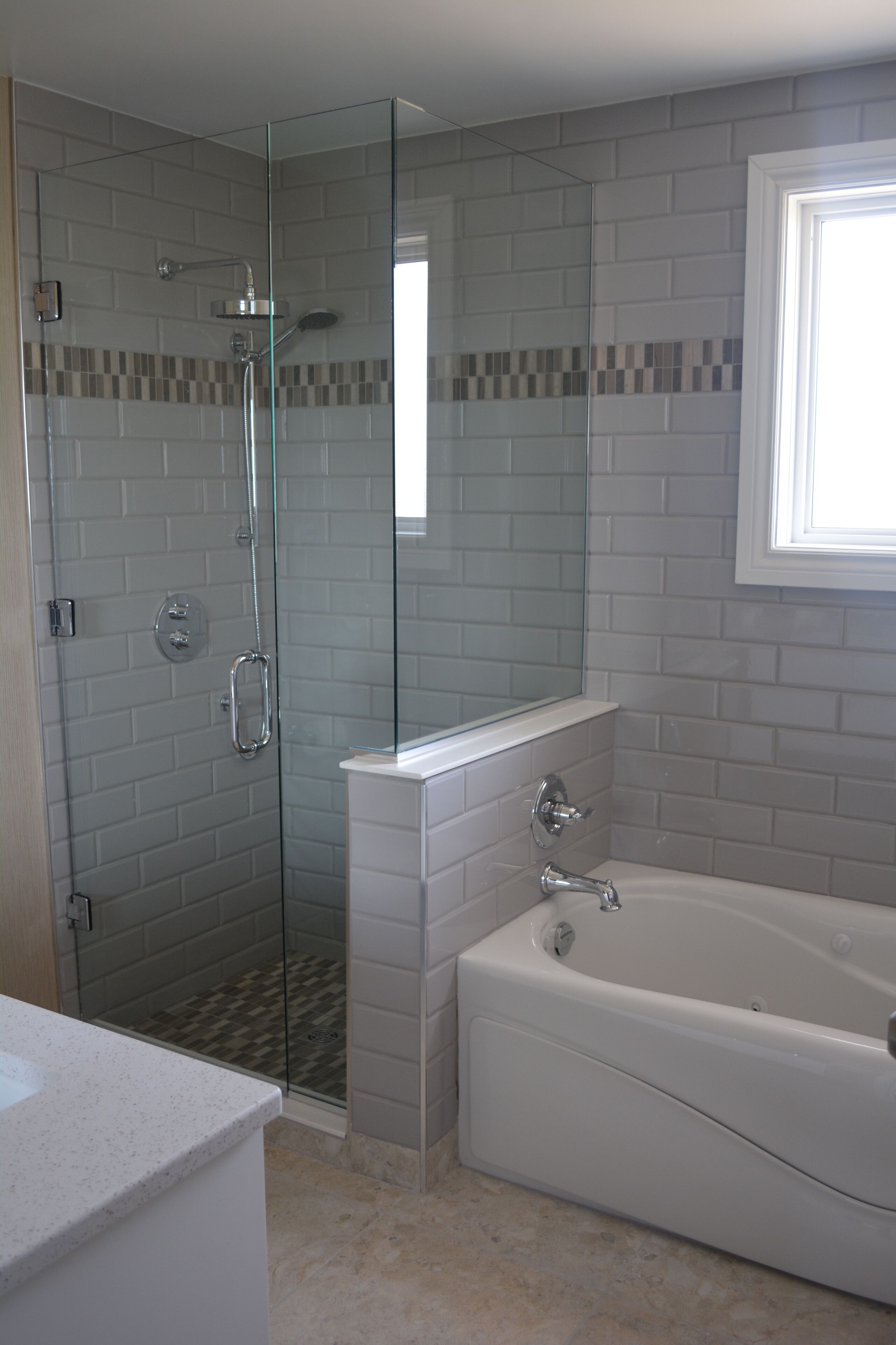 A bathroom with a glass-enclosed shower, a white bathtub, and a tiled wall with a checkered pattern.