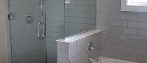 A bathroom with a glass-enclosed shower, a white bathtub, and a tiled wall with a checkered pattern.