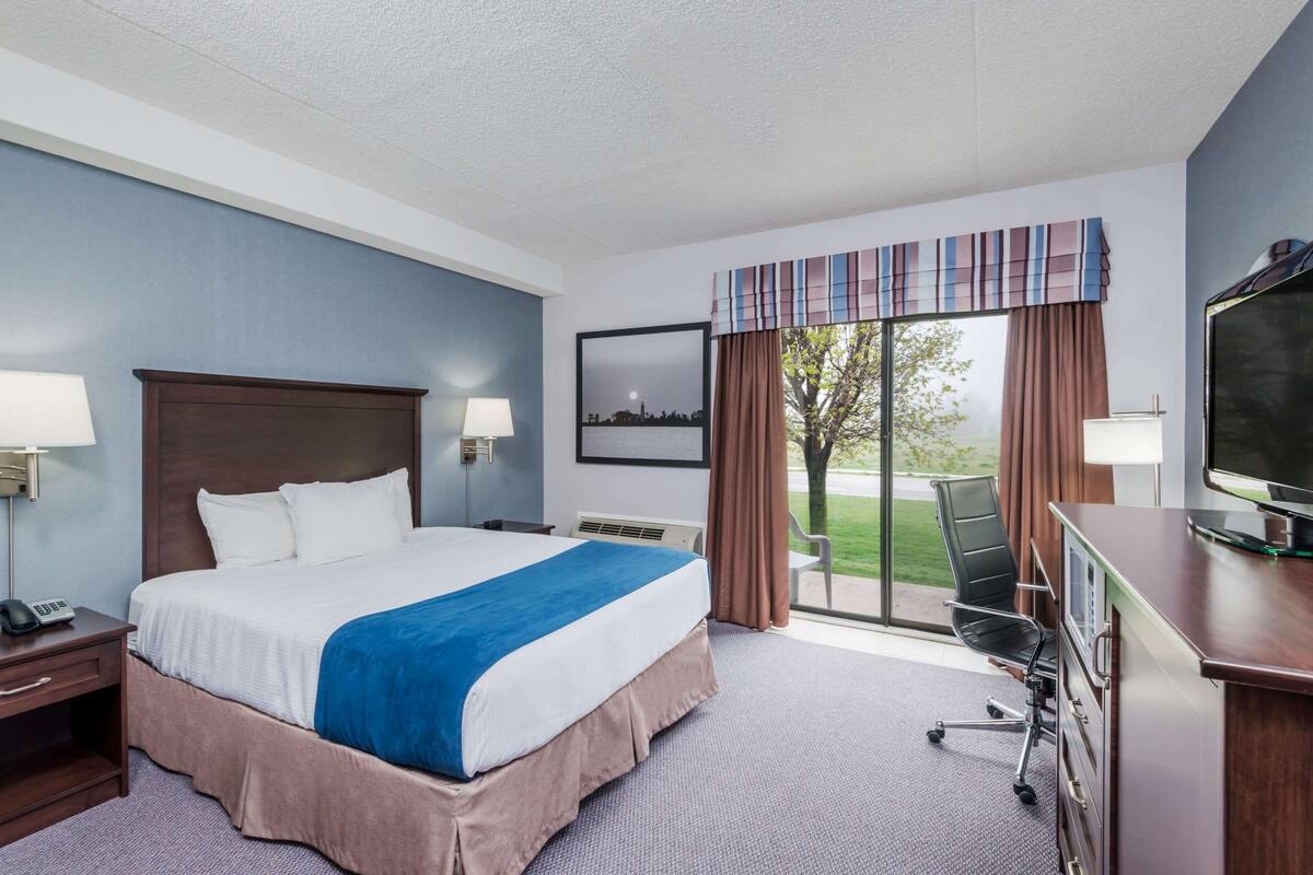 A hotel room with a large bed, a desk with a computer, a chair, and a view of the outdoors.