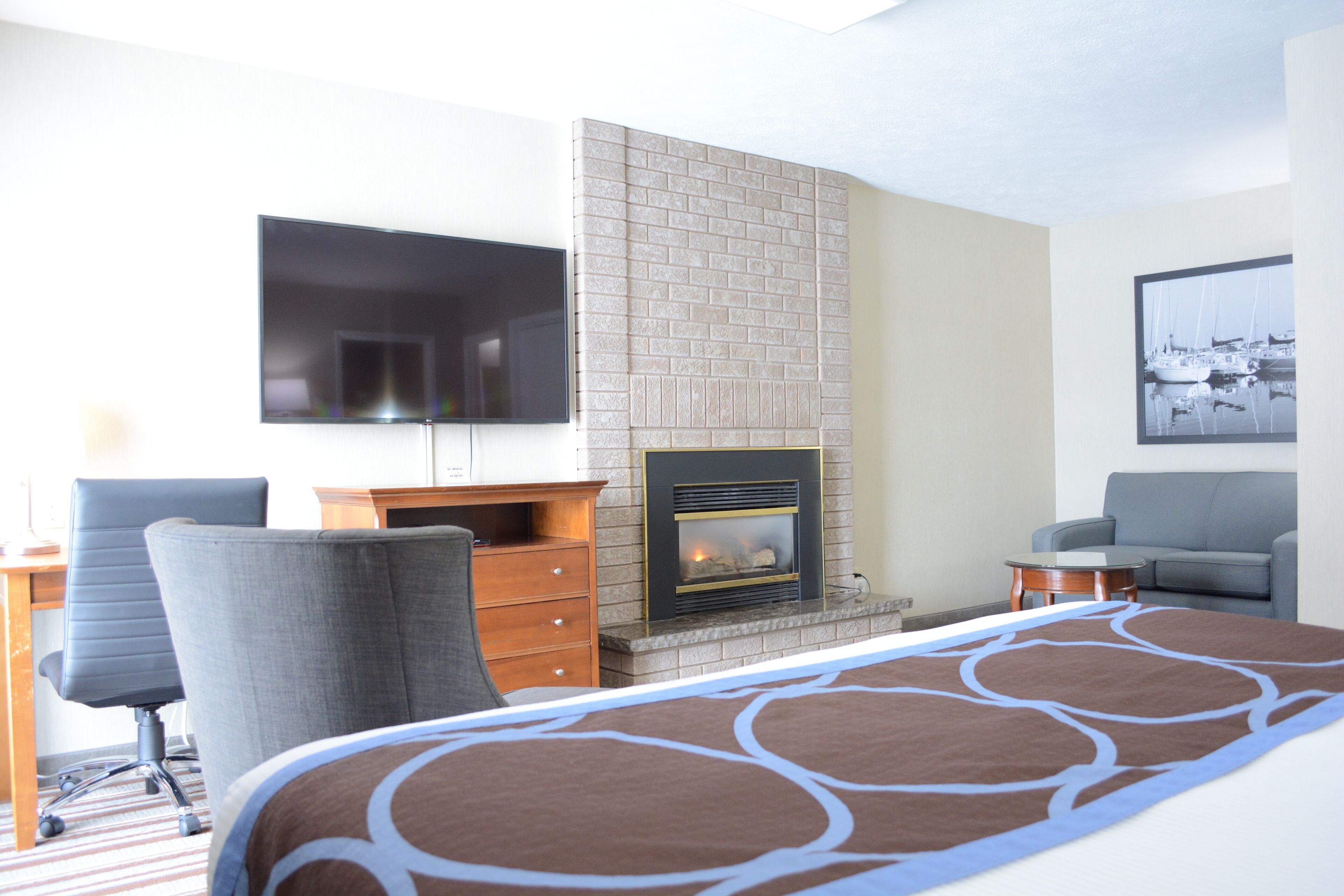 Habitación de hotel con chimenea, televisor de pantalla plana montado en la pared, escritorio con silla y sofá.