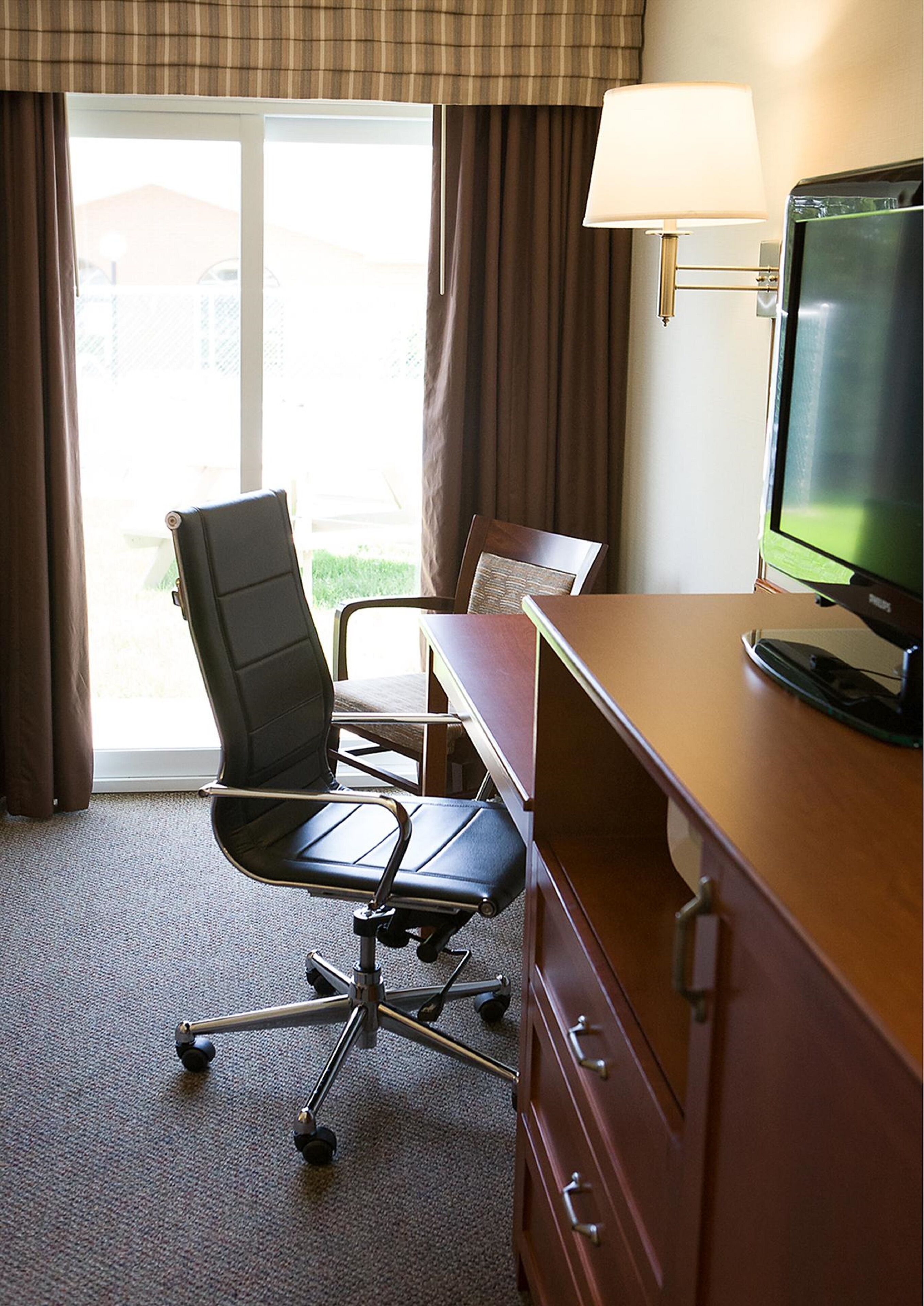 Habitación de hotel con escritorio, silla, televisión y vistas al exterior.
