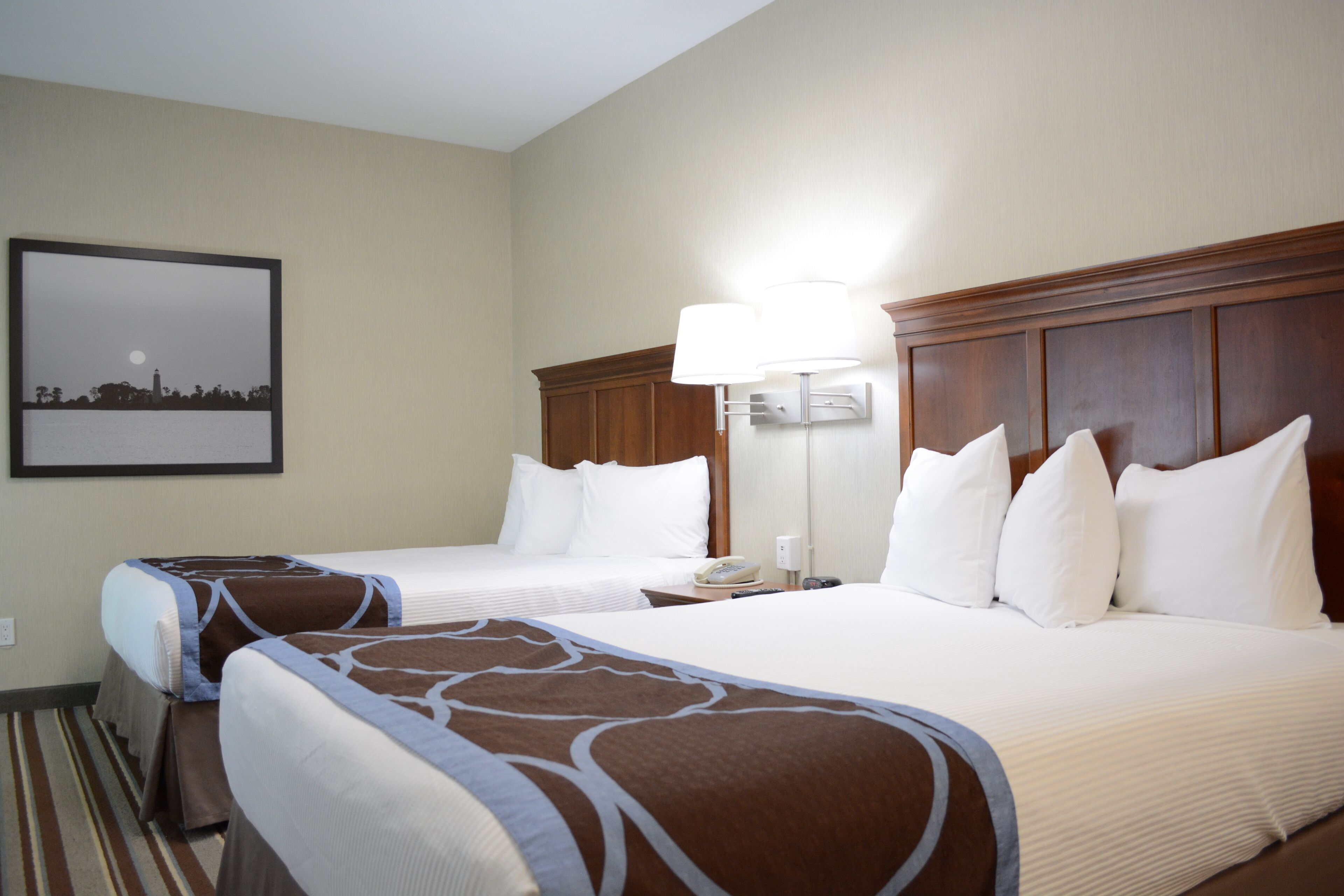 A hotel room with two beds, a nightstand, a lamp, and a framed picture on the wall.