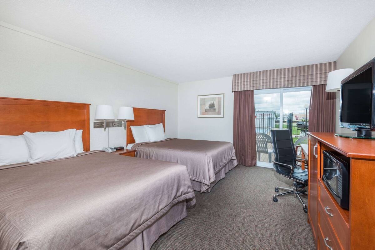 A hotel room with two beds, a desk with a television, and a view of the city through the window.