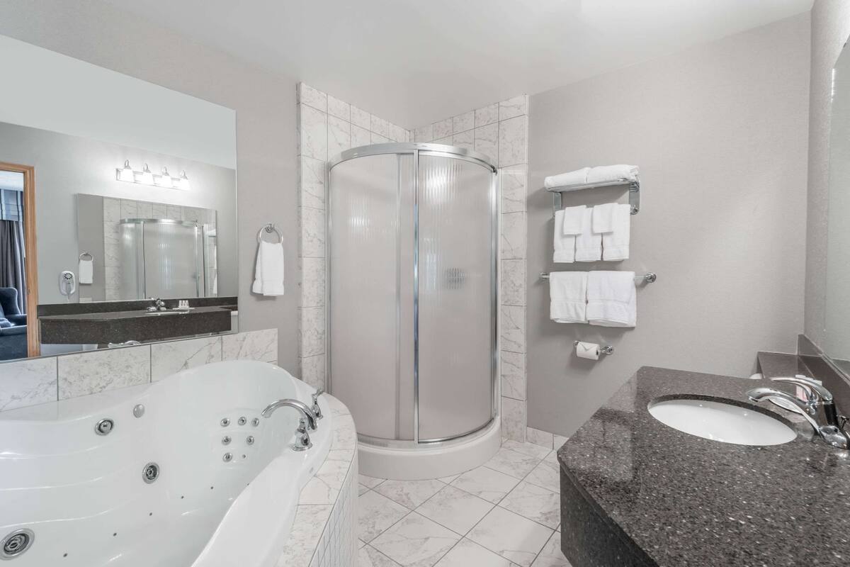 A modern bathroom with a large bathtub, a glass-enclosed shower, and a granite countertop sink.