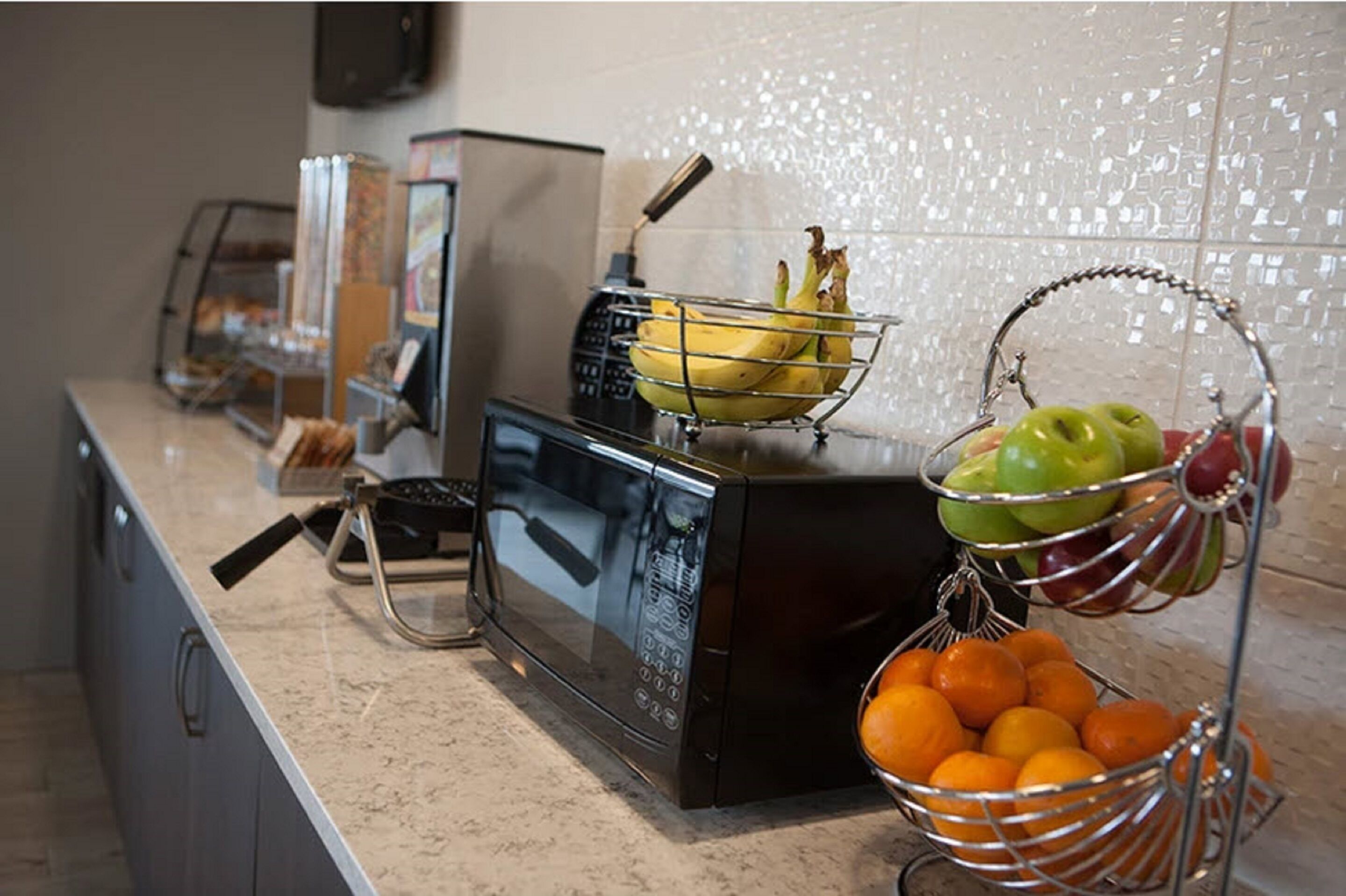 Una encimera de cocina con un microondas, una frutera con plátanos, manzanas y naranjas, y una cafetera.