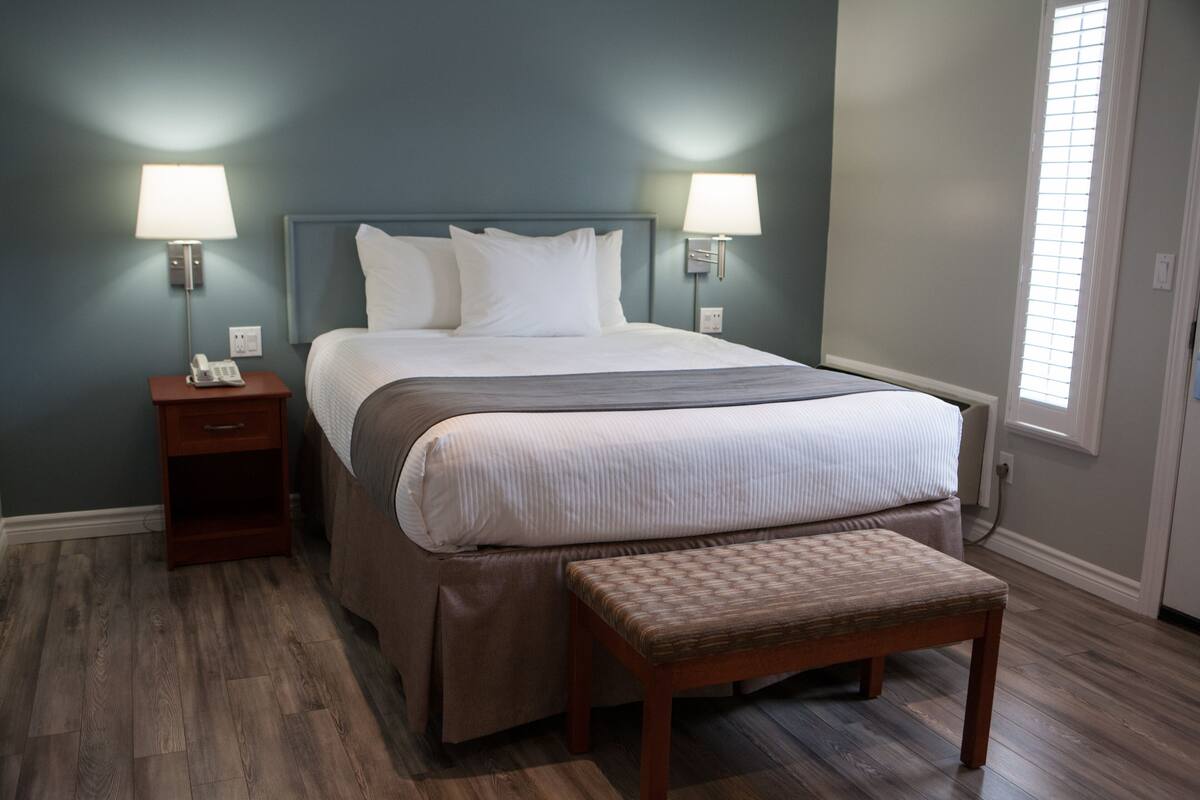 A bedroom with a bed, bedside lamps, a nightstand, and a bench.