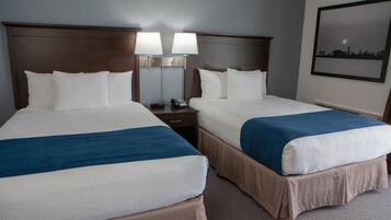 A hotel room with two beds, each with a blue and white bedspread, a nightstand with a phone, and a wall-mounted lamp.