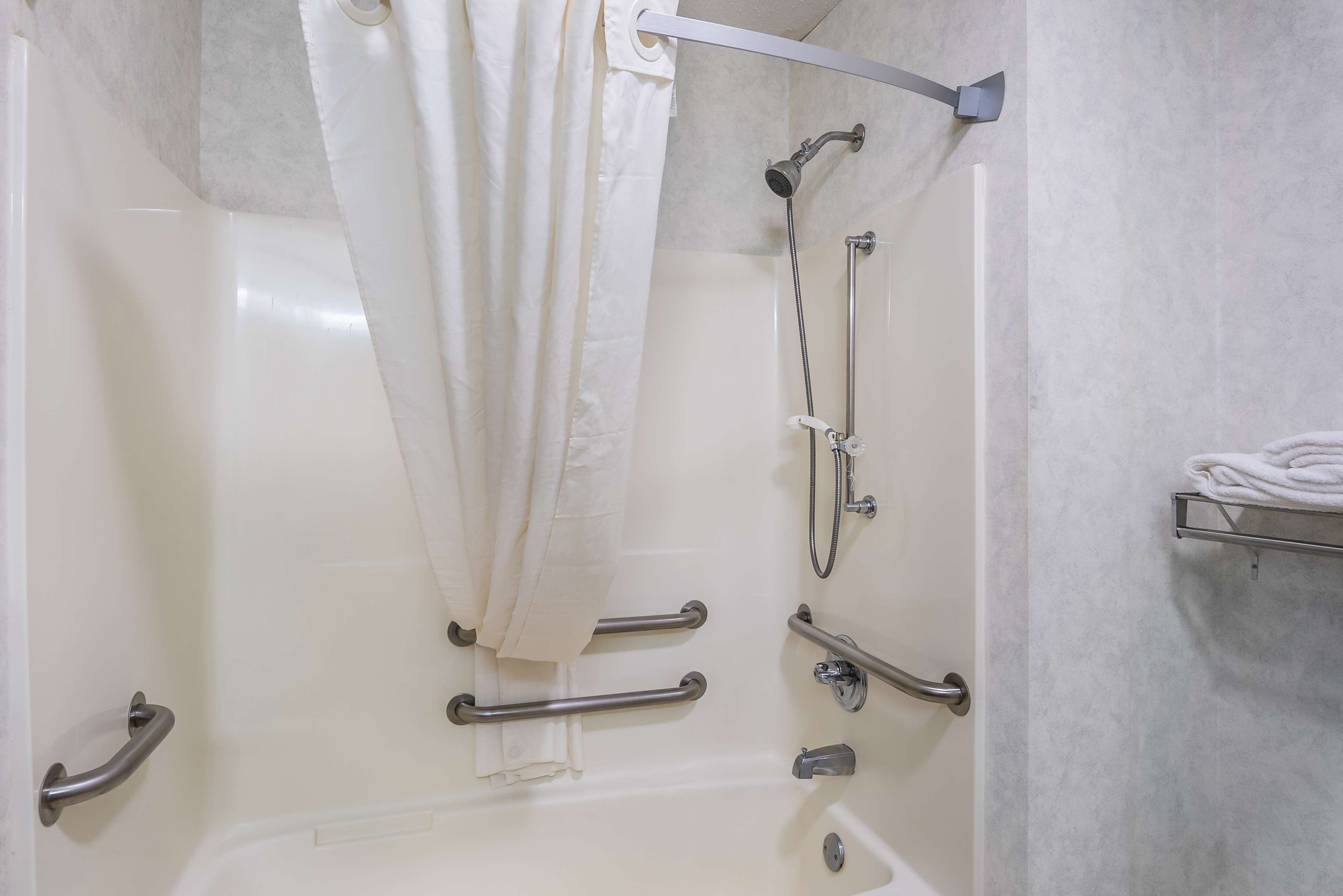 A bathroom with a bathtub, grab bars, a shower head, and a towel rack.