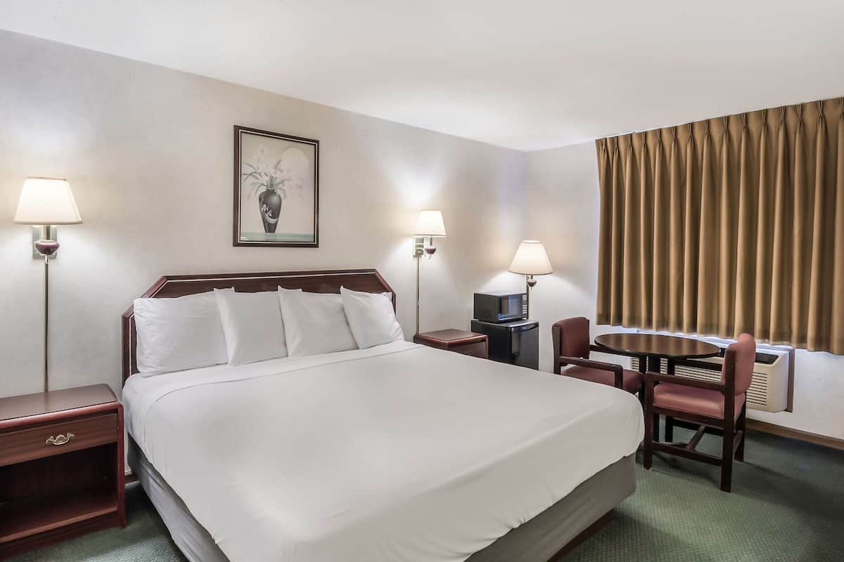 A hotel room with a large bed, two bedside tables, a desk with a chair, and a picture on the wall.