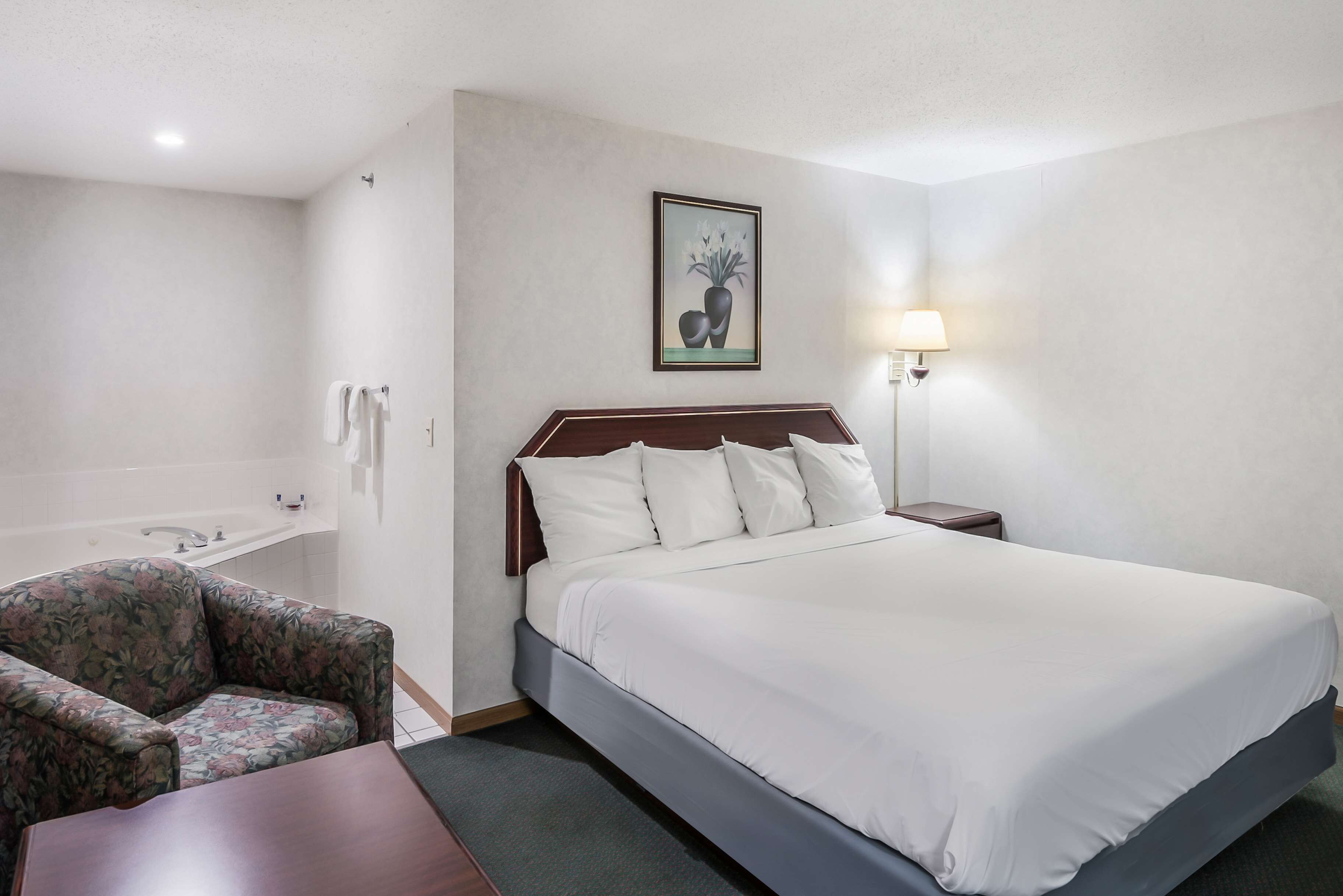 Habitación de hotel con cama, una silla, mesita de noche, lámpara y un cuadro en la pared.
