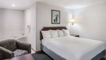Habitación de hotel con cama, una silla, mesita de noche, lámpara y un cuadro en la pared.