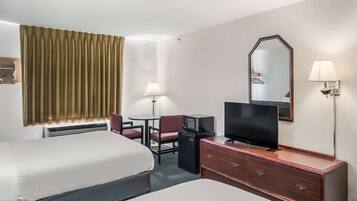 A hotel room with two beds, a desk with a television, a small refrigerator, a lamp, and a mirror.